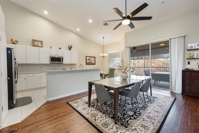 dining area with ceiling fan with notable chandelier, light hardwood / wood-style floors, and high vaulted ceiling