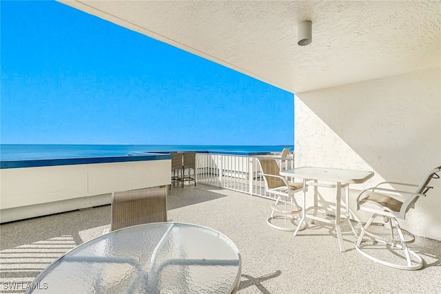 view of patio featuring a water view, a beach view, and a balcony