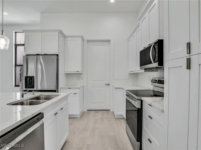 kitchen featuring light stone countertops, light hardwood / wood-style floors, pendant lighting, white cabinets, and appliances with stainless steel finishes