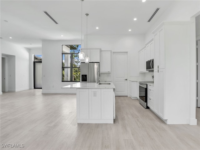 kitchen with a center island with sink, hanging light fixtures, sink, appliances with stainless steel finishes, and white cabinetry