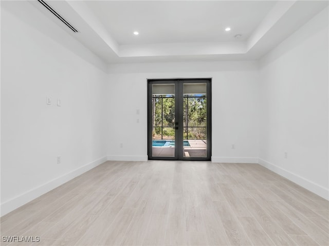 empty room with a tray ceiling, french doors, and light hardwood / wood-style flooring