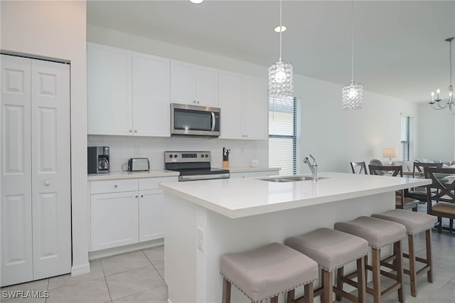 kitchen with stainless steel appliances, hanging light fixtures, sink, and an island with sink