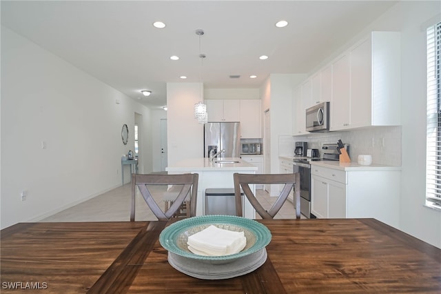 kitchen featuring pendant lighting, tasteful backsplash, a kitchen island with sink, white cabinetry, and appliances with stainless steel finishes