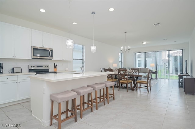 kitchen with stainless steel appliances, a center island with sink, white cabinets, hanging light fixtures, and sink