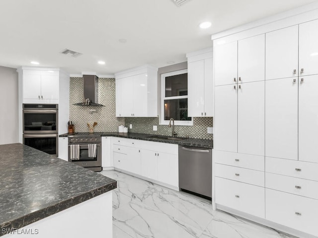 kitchen featuring white cabinetry, appliances with stainless steel finishes, decorative backsplash, and wall chimney exhaust hood