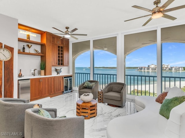 living room featuring built in shelves, sink, beverage cooler, a water view, and ceiling fan