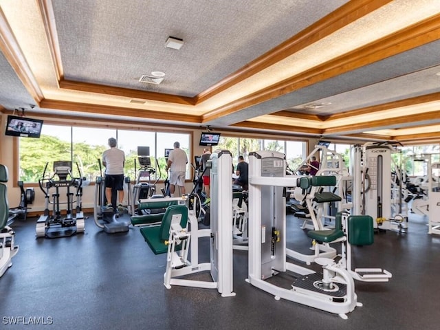 gym with ornamental molding, a textured ceiling, and a raised ceiling