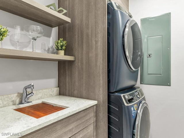 laundry area featuring electric panel, sink, and stacked washer / drying machine