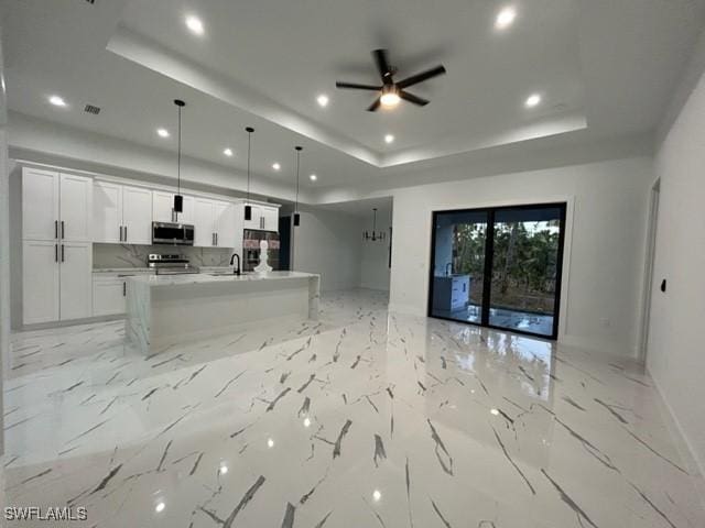 kitchen featuring stainless steel appliances, white cabinetry, hanging light fixtures, and a tray ceiling