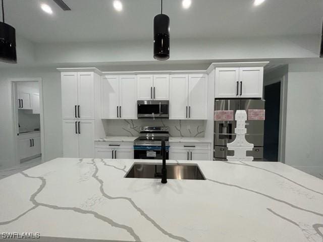 kitchen with decorative light fixtures, stainless steel appliances, white cabinetry, and light stone counters