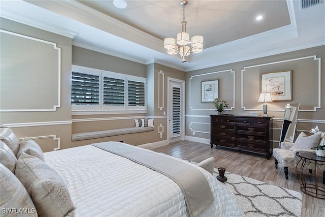 bedroom featuring light wood-type flooring, crown molding, a chandelier, and a tray ceiling