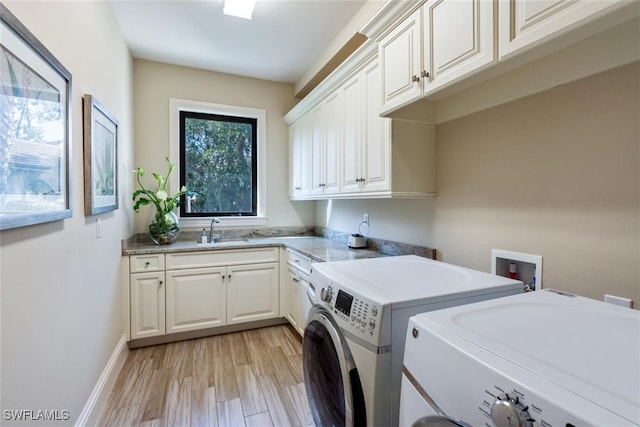 clothes washing area featuring sink, washer and clothes dryer, light hardwood / wood-style floors, and cabinets