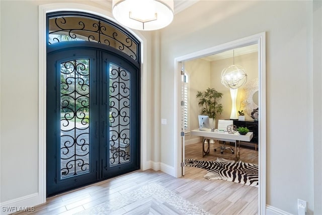 foyer with light wood-type flooring, french doors, crown molding, and a chandelier