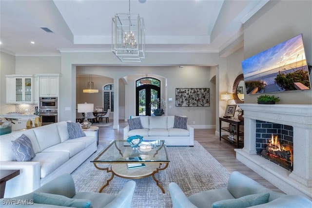 living room featuring a high end fireplace, an inviting chandelier, light wood-type flooring, and ornamental molding