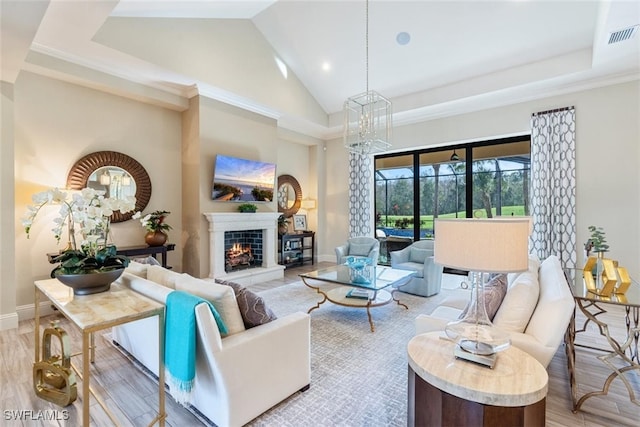 living room with ornamental molding, high vaulted ceiling, light wood-type flooring, and an inviting chandelier