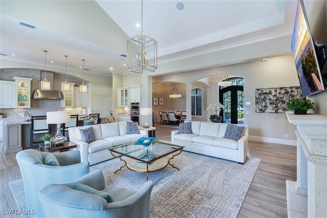 living room with a high ceiling, light wood-type flooring, ornamental molding, and a chandelier