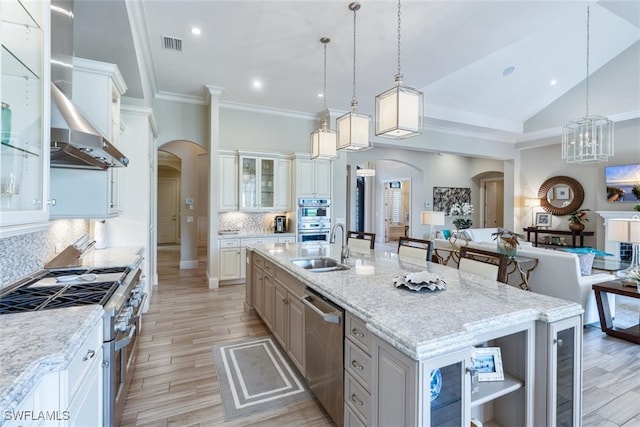 kitchen featuring stainless steel appliances, an island with sink, sink, decorative light fixtures, and backsplash