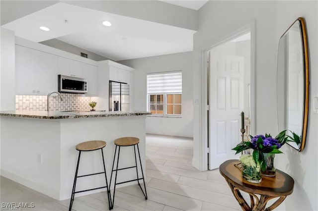 kitchen with white cabinets, kitchen peninsula, appliances with stainless steel finishes, and light stone counters