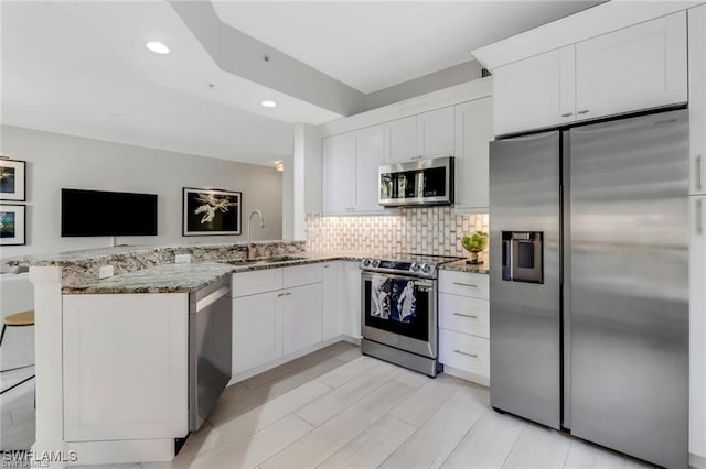 kitchen featuring kitchen peninsula, light stone countertops, white cabinetry, and appliances with stainless steel finishes