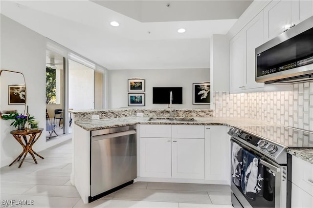 kitchen with tasteful backsplash, light stone counters, white cabinetry, appliances with stainless steel finishes, and kitchen peninsula