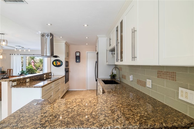 kitchen featuring island exhaust hood, dark stone counters, white cabinetry, sink, and kitchen peninsula