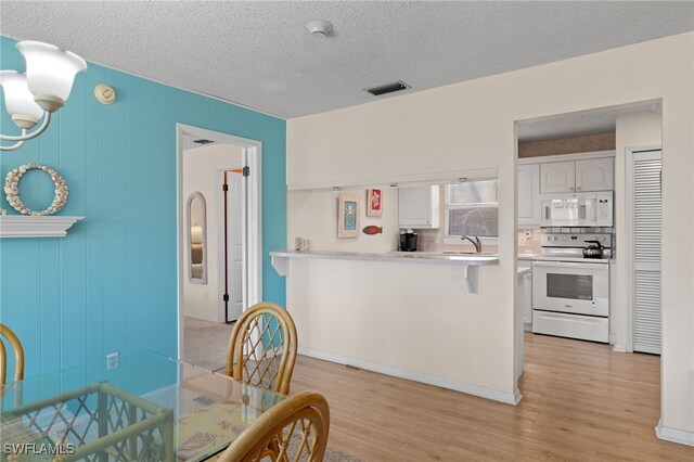 dining space with a textured ceiling, light hardwood / wood-style floors, and wooden walls