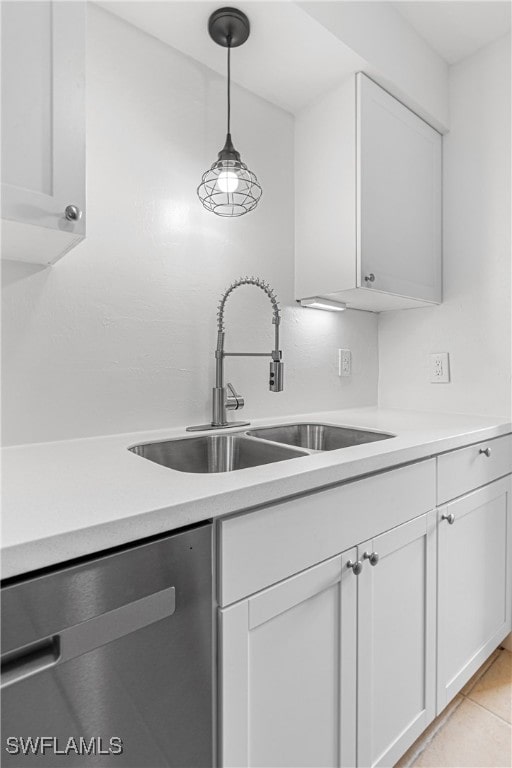 kitchen featuring sink, light tile patterned floors, stainless steel dishwasher, hanging light fixtures, and white cabinets