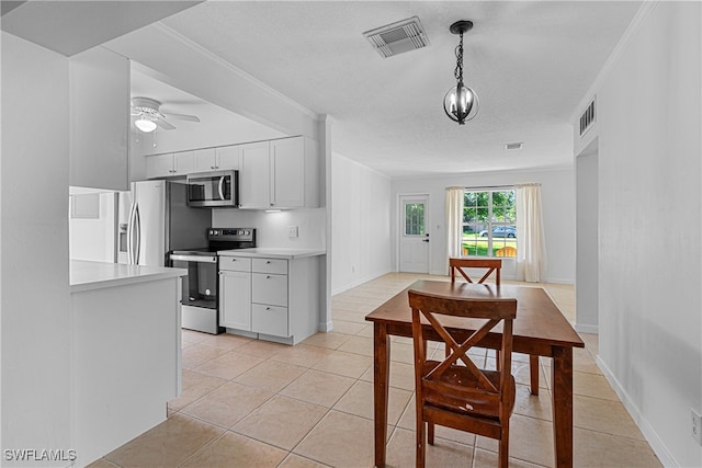 kitchen with pendant lighting, light tile patterned flooring, crown molding, white cabinetry, and appliances with stainless steel finishes