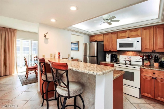 kitchen with a kitchen bar, kitchen peninsula, white appliances, ceiling fan, and crown molding