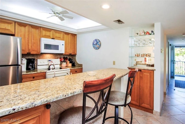 kitchen featuring light stone counters, a breakfast bar, ceiling fan, and white appliances