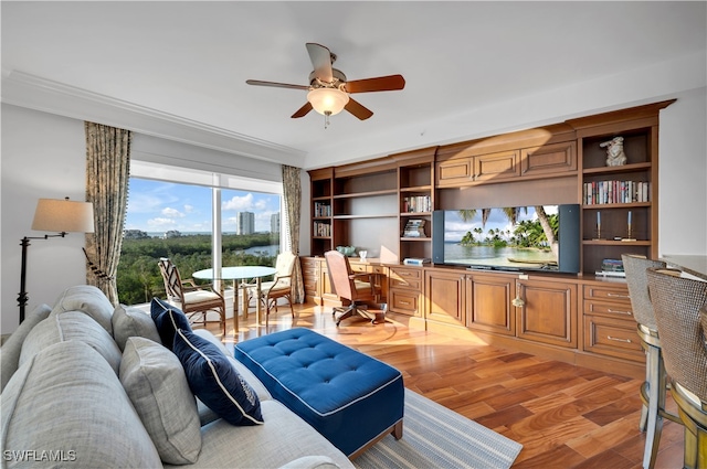 living room featuring crown molding, light wood-type flooring, built in desk, and ceiling fan