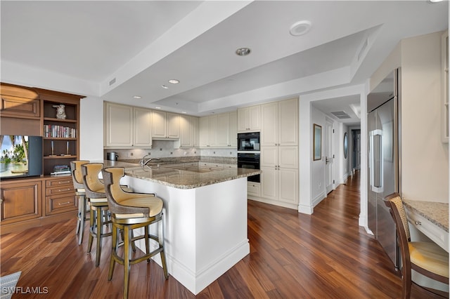 kitchen featuring dark wood-type flooring, an island with sink, light stone counters, and a breakfast bar area