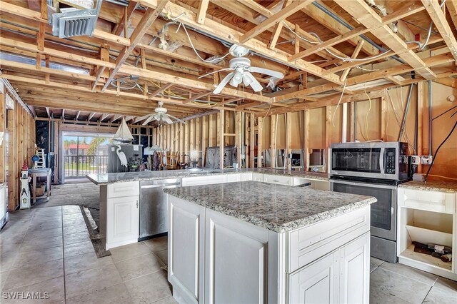 kitchen featuring white cabinetry, appliances with stainless steel finishes, light stone counters, ceiling fan, and a kitchen island