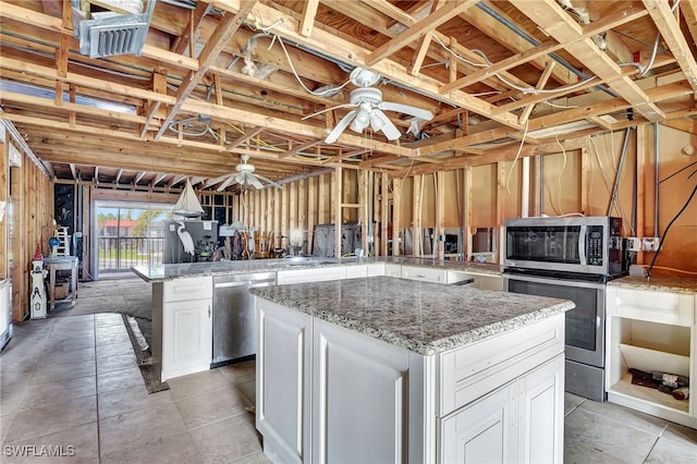 kitchen featuring a kitchen island, appliances with stainless steel finishes, white cabinets, light stone counters, and ceiling fan