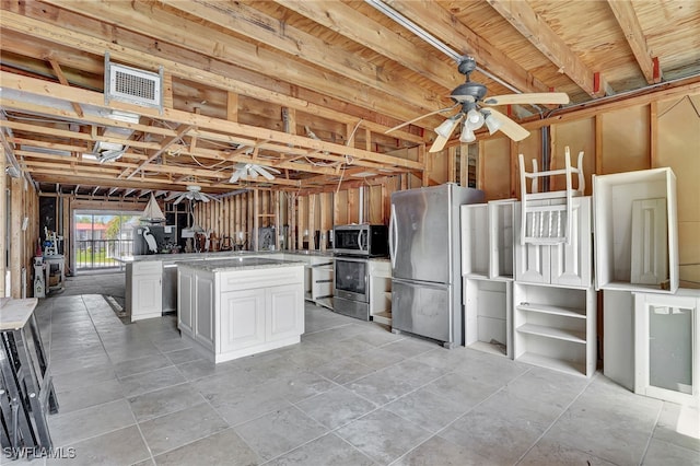 kitchen with ceiling fan, a kitchen island, light stone countertops, white cabinetry, and appliances with stainless steel finishes