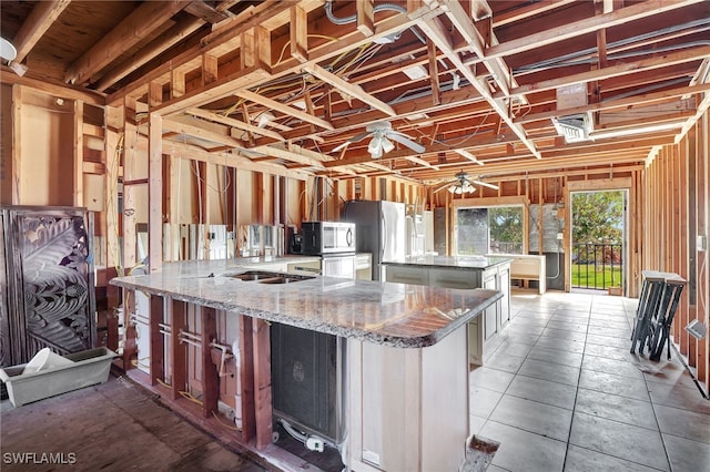 kitchen with a kitchen island, light stone counters, ceiling fan, and stainless steel appliances