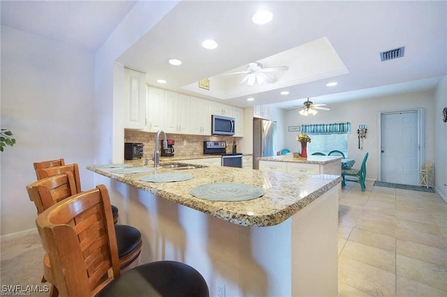 kitchen with white cabinetry, sink, appliances with stainless steel finishes, kitchen peninsula, and a raised ceiling