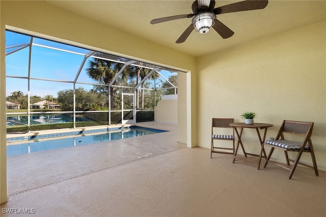 view of swimming pool with ceiling fan, glass enclosure, and a patio area