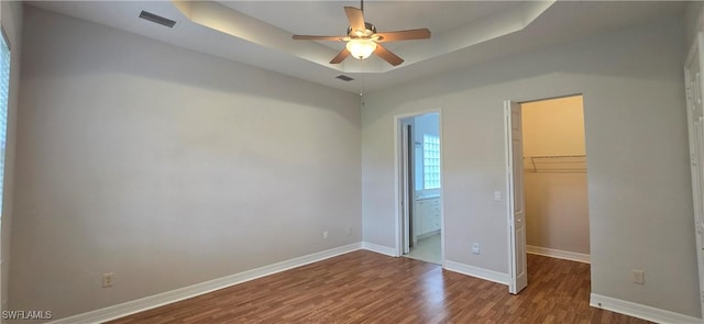 unfurnished bedroom featuring ceiling fan, hardwood / wood-style floors, a tray ceiling, a spacious closet, and a closet