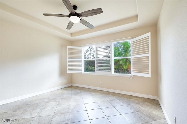 empty room with light tile patterned flooring, ceiling fan, and a raised ceiling