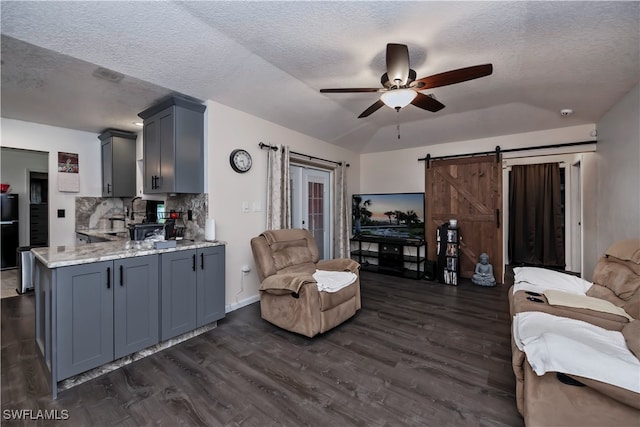 living room with ceiling fan, dark hardwood / wood-style floors, a textured ceiling, and a barn door