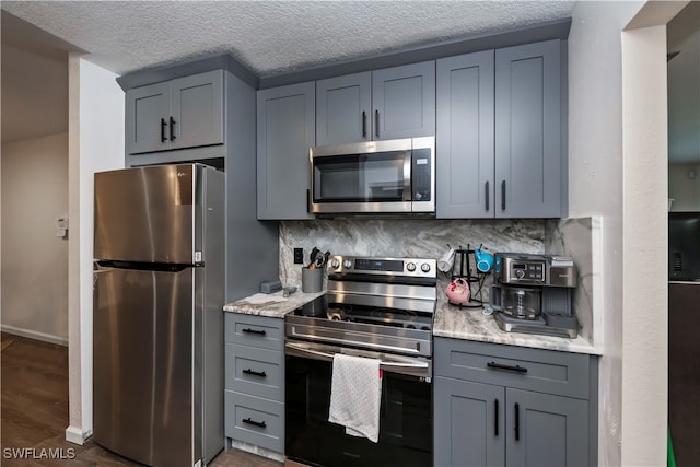 kitchen featuring dark hardwood / wood-style flooring, stainless steel appliances, a textured ceiling, backsplash, and light stone countertops