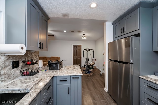 kitchen with gray cabinetry, backsplash, a textured ceiling, stainless steel refrigerator, and dark hardwood / wood-style flooring