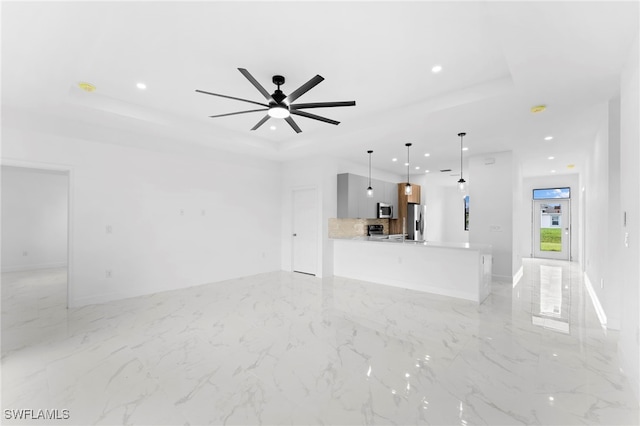 unfurnished living room featuring ceiling fan and a tray ceiling