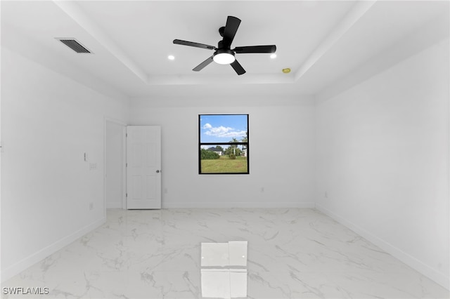 empty room with ceiling fan and a tray ceiling