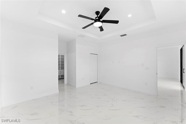 spare room with ceiling fan and a tray ceiling