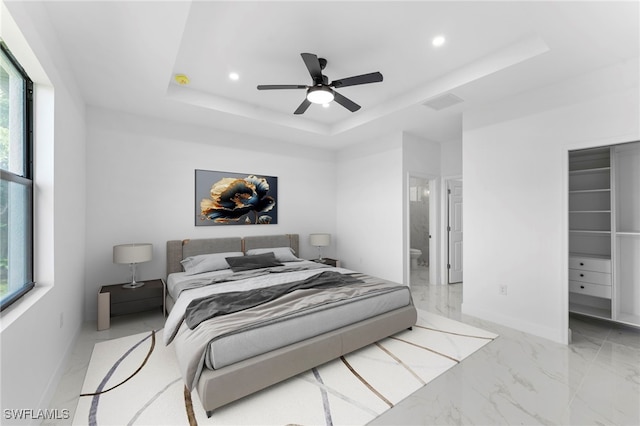 bedroom featuring ceiling fan, a tray ceiling, and ensuite bath