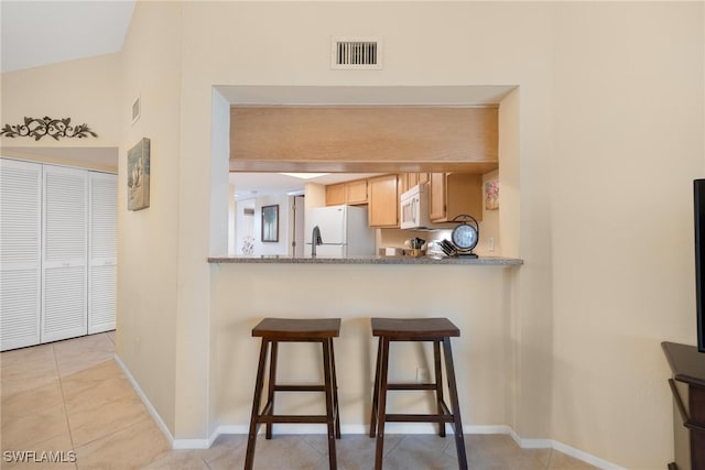 kitchen with stone countertops, kitchen peninsula, light tile patterned floors, white appliances, and vaulted ceiling