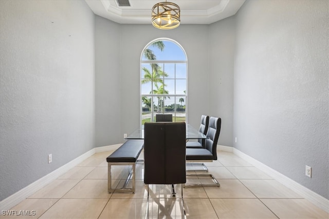 tiled dining space with ornamental molding and a tray ceiling