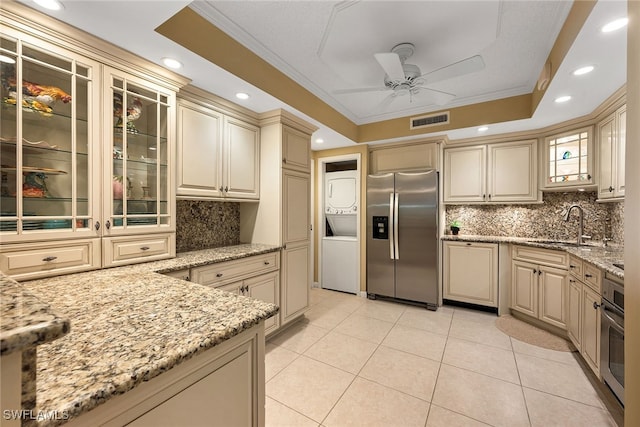 kitchen with light stone counters, sink, crown molding, appliances with stainless steel finishes, and cream cabinetry